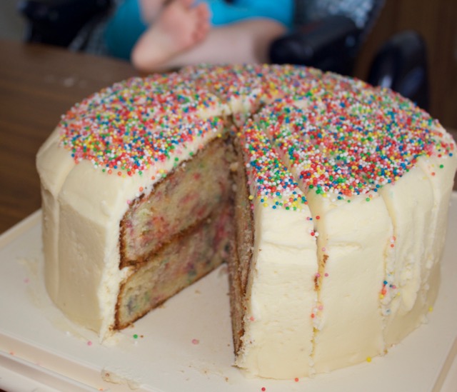 Birthday cake with sprinkles. Small child in the background.