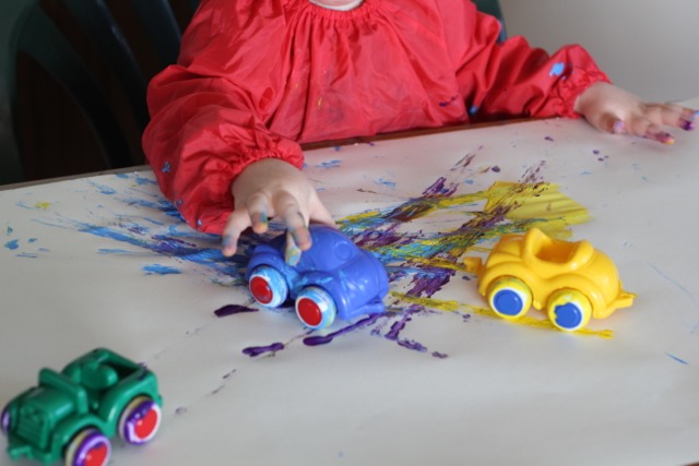 Child using toy vehicles to paint with.