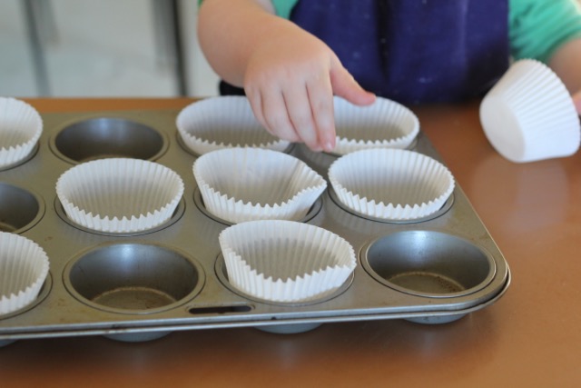 child placing cupcake cases into tray