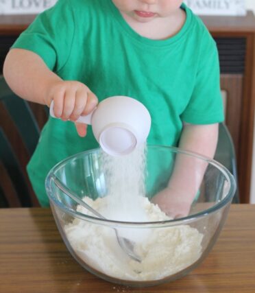 Small child pouring coconut into a bowl of cake ingredients