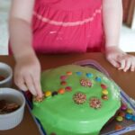 Child decorating cake with green icing and various lollies